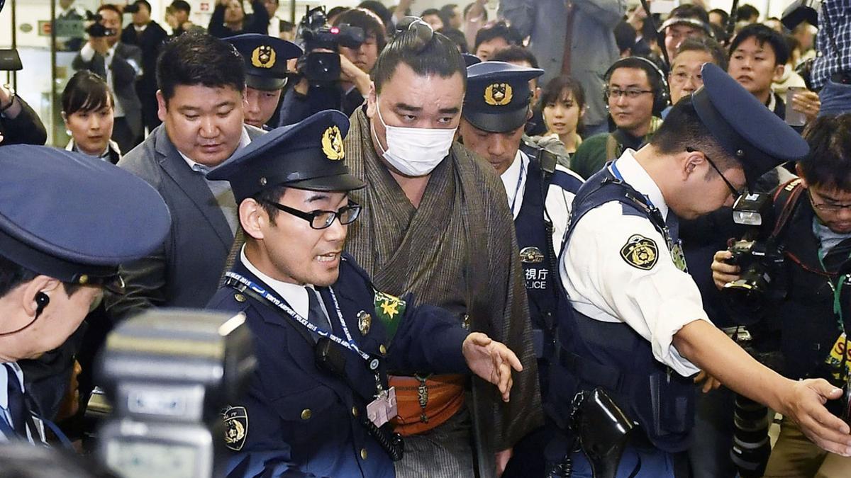 Mongolian-born grand sumo champion Yokozuna Harumafuji is escorted by police officers upon his arrival at Haneda airport in Tokyo