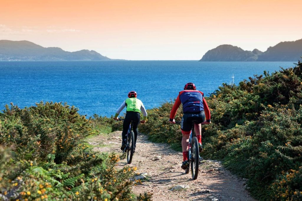 Ciclistas con las islas Cíes al fondo y excursionistas rumbo a la Pedra da Campá