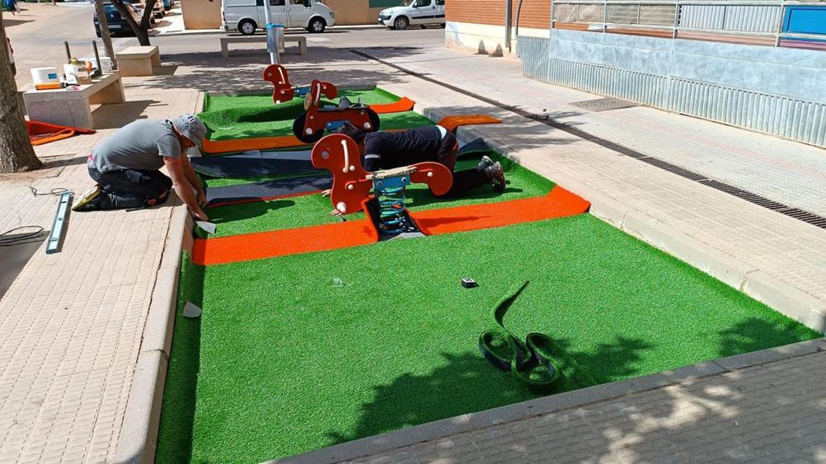 Operarios colocan el nuevo césped artificial en un parque infantil