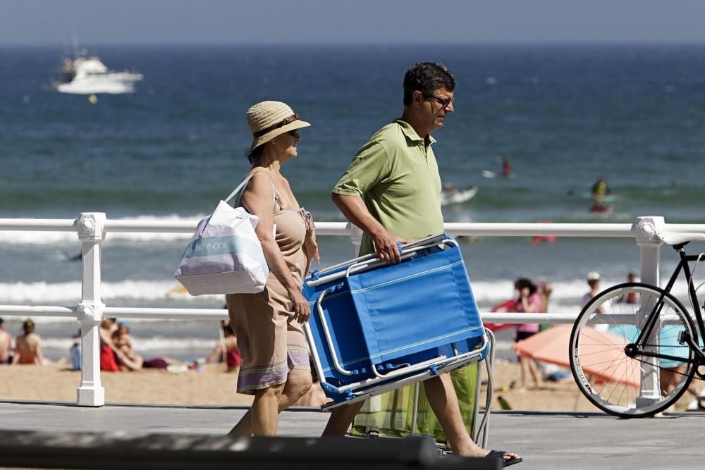 Gijoneses y visitantes se lanzan a la playa en una jornada calurosa.