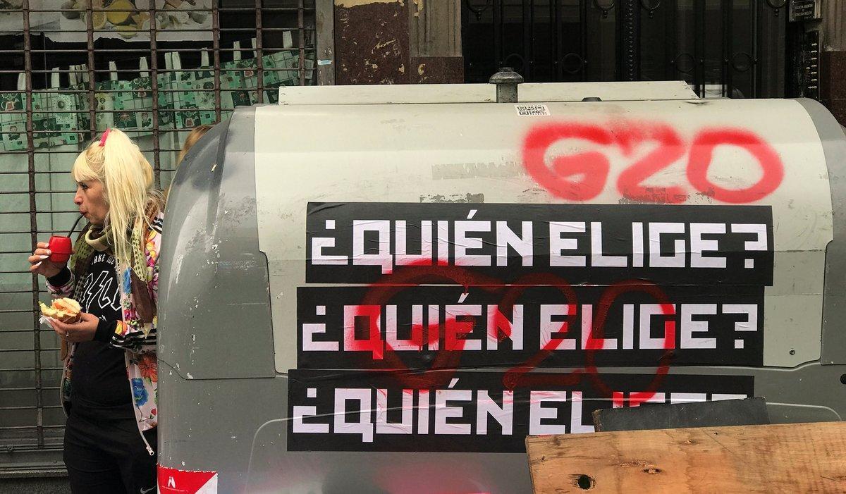 A woman drinks traditional Argentine mate drink as she stands next to a dumpster with signs and graffiti that read  Who chooses   and G20 in Buenos Aires  Argentina November 23  2018  REUTERS Marcos Brindicci