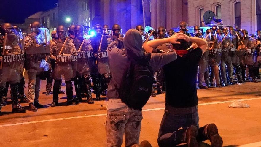 Dos hombres se arrodillan frente a una línea de la policía estatal de Kentucky.