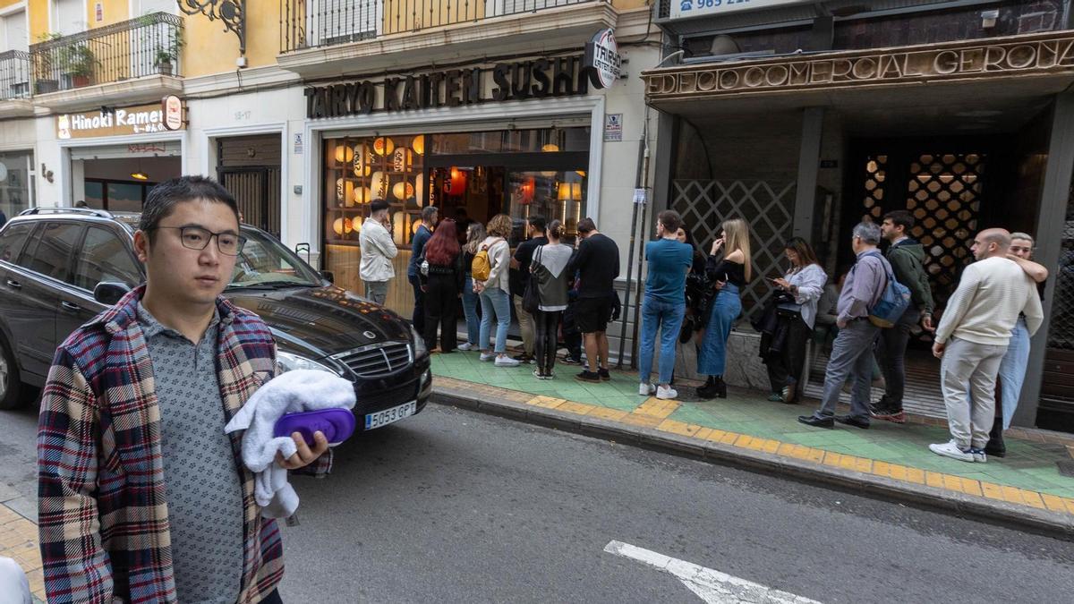 Una familia pasa frente a la cola de un restaurante asiático en la calle Gerona de Alicante.