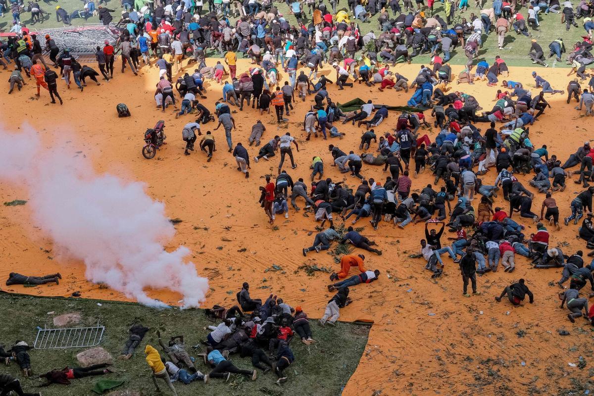 EDITORS NOTE: Graphic content / TOPSHOT - Supporters and mourners of Kenyan opposition leader Raila Odinga run for cover after gunshots and teargas were fired during a gathering for the public viewing of his coffin at the Kasarani Stadium in Nairobi on October 16, 2025 following Odingas death at the age of 80 during a health visit to India. Tens of thousands of mourners fled in panic as police fired gunshots and teargas in a stadium where they had gathered to see the coffin of opposition leader Raila Odinga, whose body was repatriated from India on October 16, 2025. (Photo by KABIR DHANJI / AFP). Graphic content