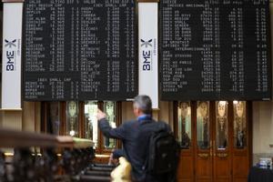 Un hombre señala los paneles de valores del IBEX 35 en el Palacio de la Bolsa de Madrid