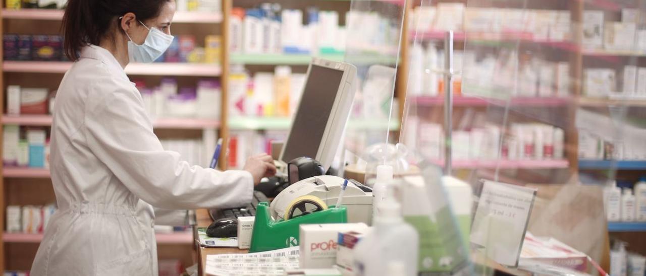 Una farmacéutica con mascarilla despacha en una farmacia.