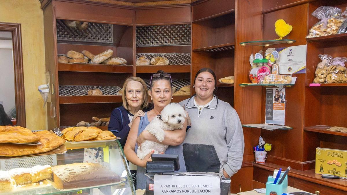 Begoña Carril, en el centro, junto a su perrita Luna, acompañada por la clienta Pilar Medina, a la izquierda, y la empleada Antía Rouco en el último día de la panadería Moure en el barrio de O Castiñeiriño.