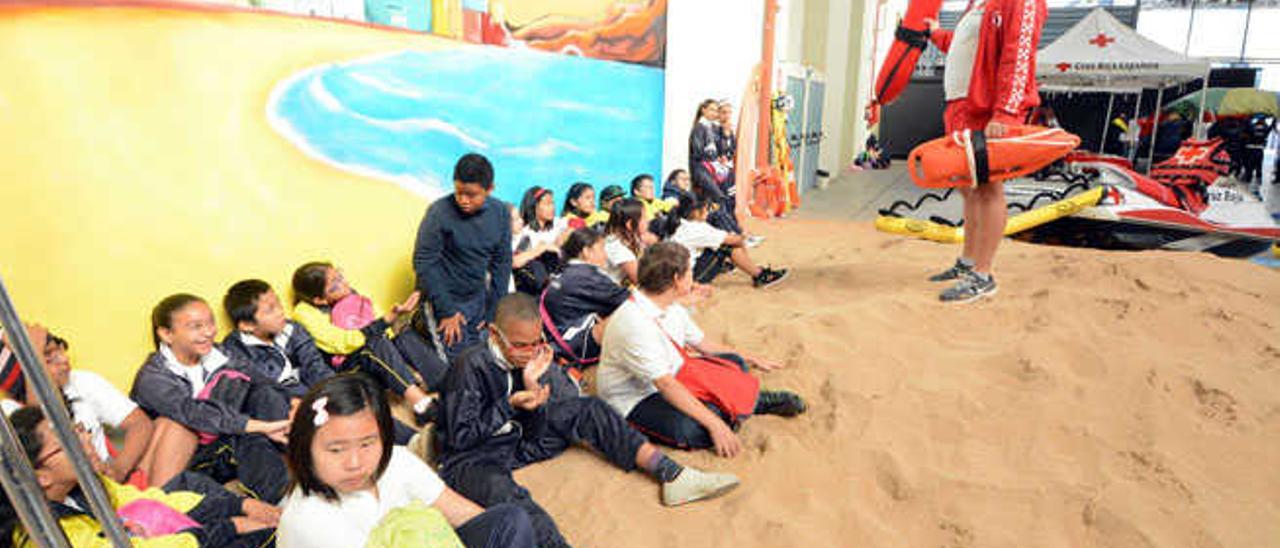 Escolares sentados en el escenario de la playa recibiendo instrucciones de socorrismo.