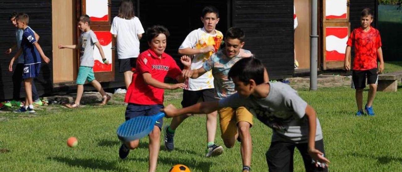 Un grupo de niños jugando al fútbol y al tenis delante de las cabañas de la escuela de fútbol rojiblanca.