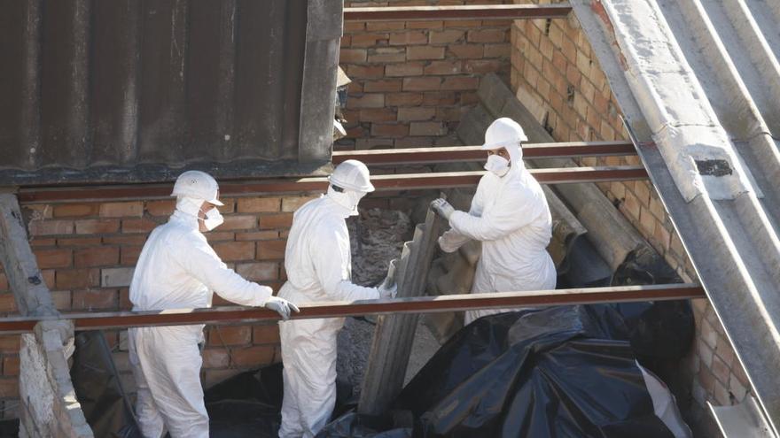 Varios operarios retiran amianto del tejado de un edificio de Murcia.