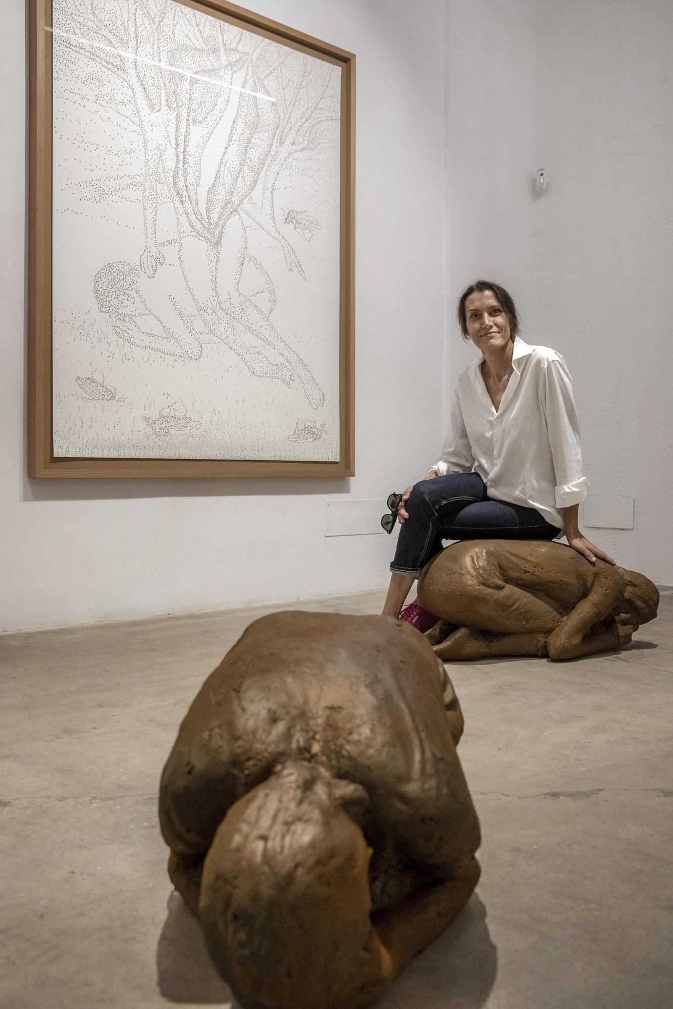 La artista posa sobre una de sus esculturas de mujer.