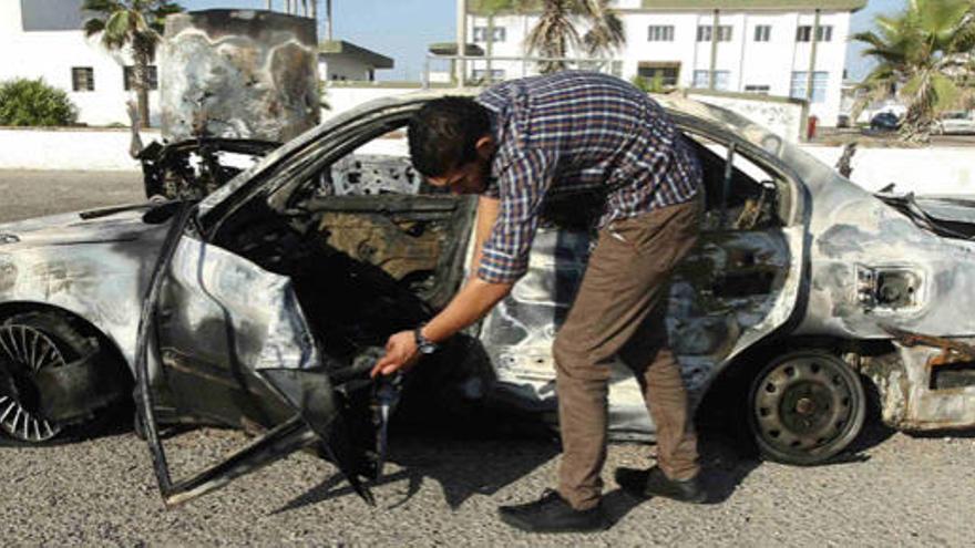 Un hombre inspecciona el coche explosionado.