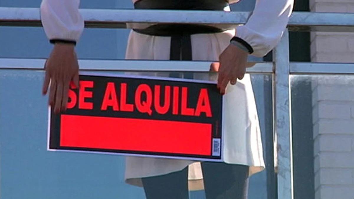 Imagen de archivo de una persona colocando un cartel de «Se alquila» en una vivienda.