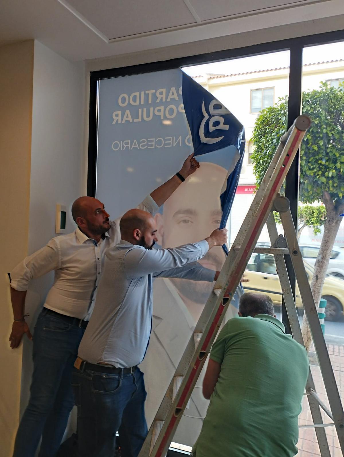 El candidato excluido, junto a dos colaboradores, retirando uno de los carteles con su foto de la sede electoral de l'Alfàs.