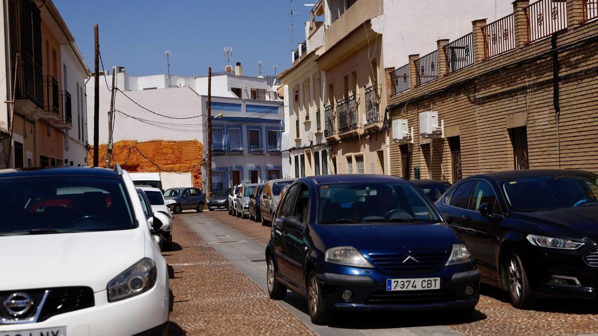 Un coche circula por una calle de Campo de la Verdad repleta de vehículos aparcados en la acera.