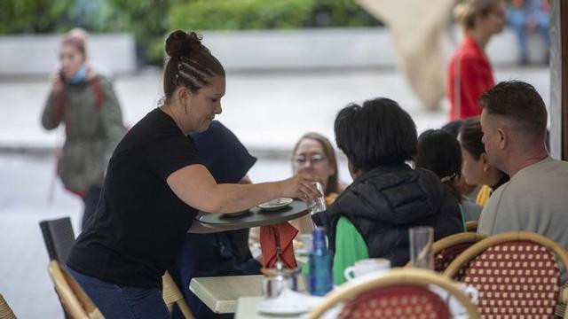 Una camarera atiende a unos clientes en la terraza.
