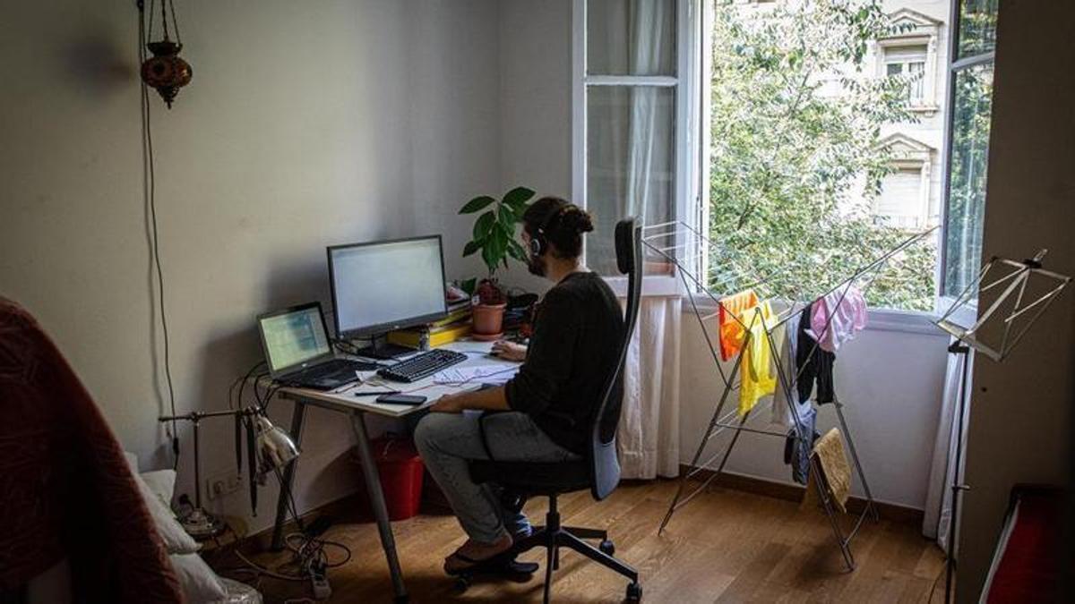 Un joven teletrabajando sobre un escritorio de una habitación de su casa.