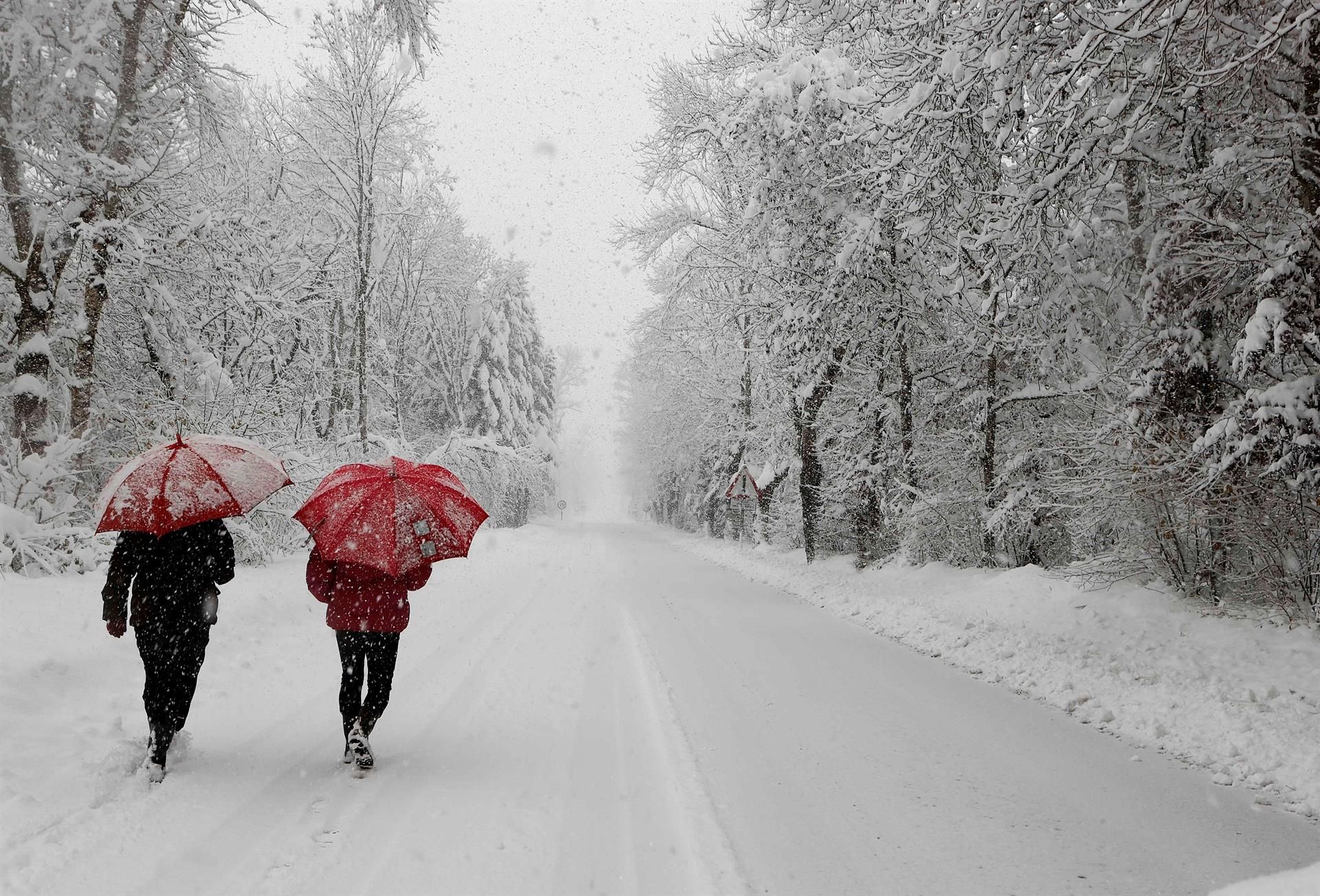 Dos personas caminan por la N-135 en Roncesvalles, Navarra, completamente cubierta de nieve, después de que este domingo el temporal haya dejado más de 40 cm de nieve.