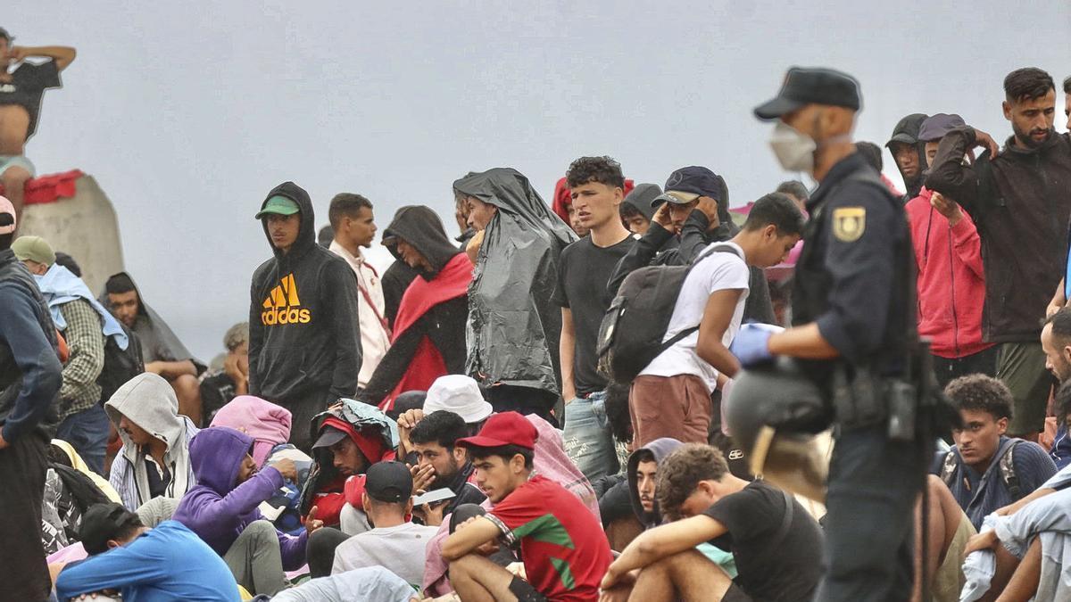 La policía vigila a inmigrantes que continúan viviendo en las inmediaciones de la playa del Trampolín en Ceuta, este viernes. El secretario de Estado Juventud e Infancia, Rubén Pérez Correa, ha considerado "factible" llevar a cabo "en un plazo de pocas semanas" el traslado de 500 niñas migrantes no acompañadas desde Ceuta a la Península y, para ello, confía en la "voluntad" del Gobierno de la ciudad autónoma. EFE/Reduan