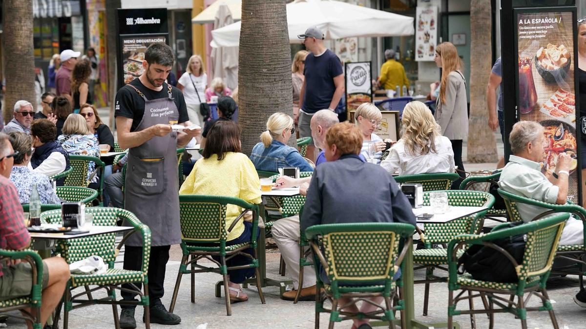 Varios camareros jóvenes sirven a los clientes en las terrazas de los restaurantes en el Centro de Málaga.