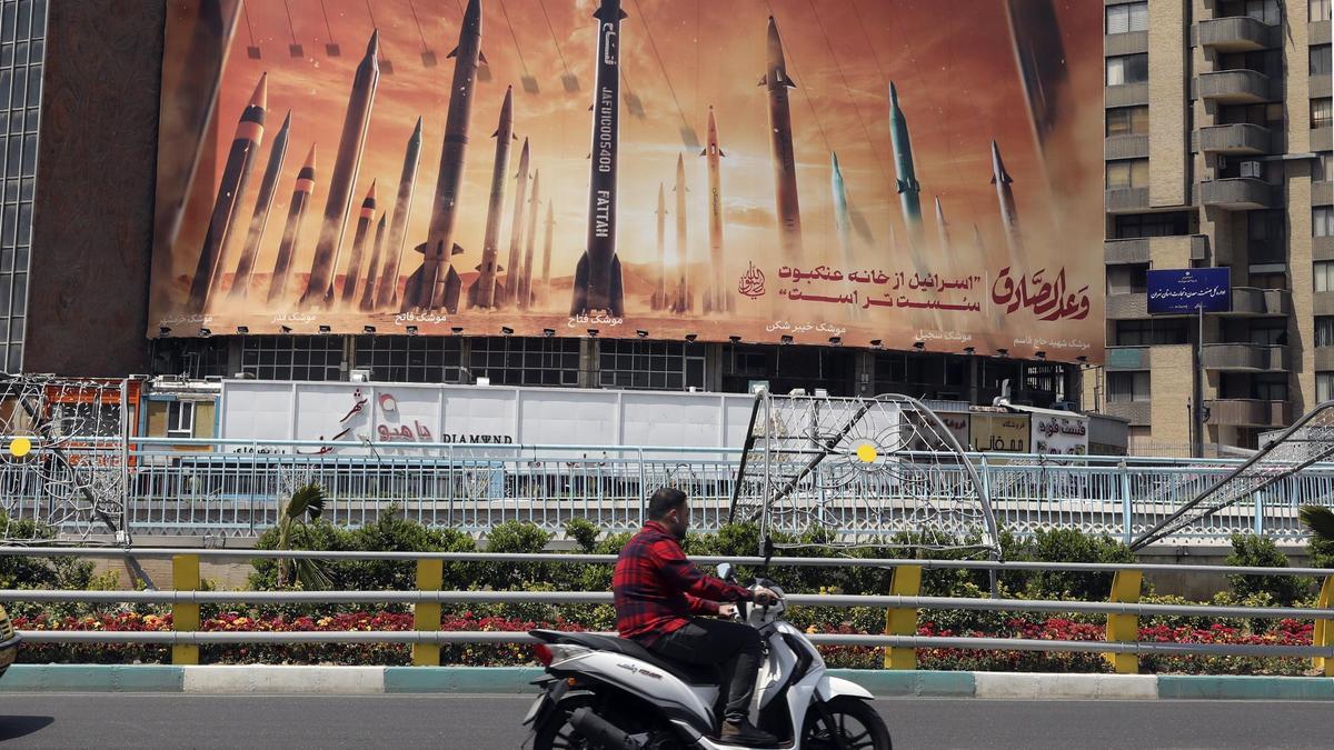 Un hombre pasa junto a una valla publicitaria antiisraelí con imágenes de misiles iraníes en Teherán,.