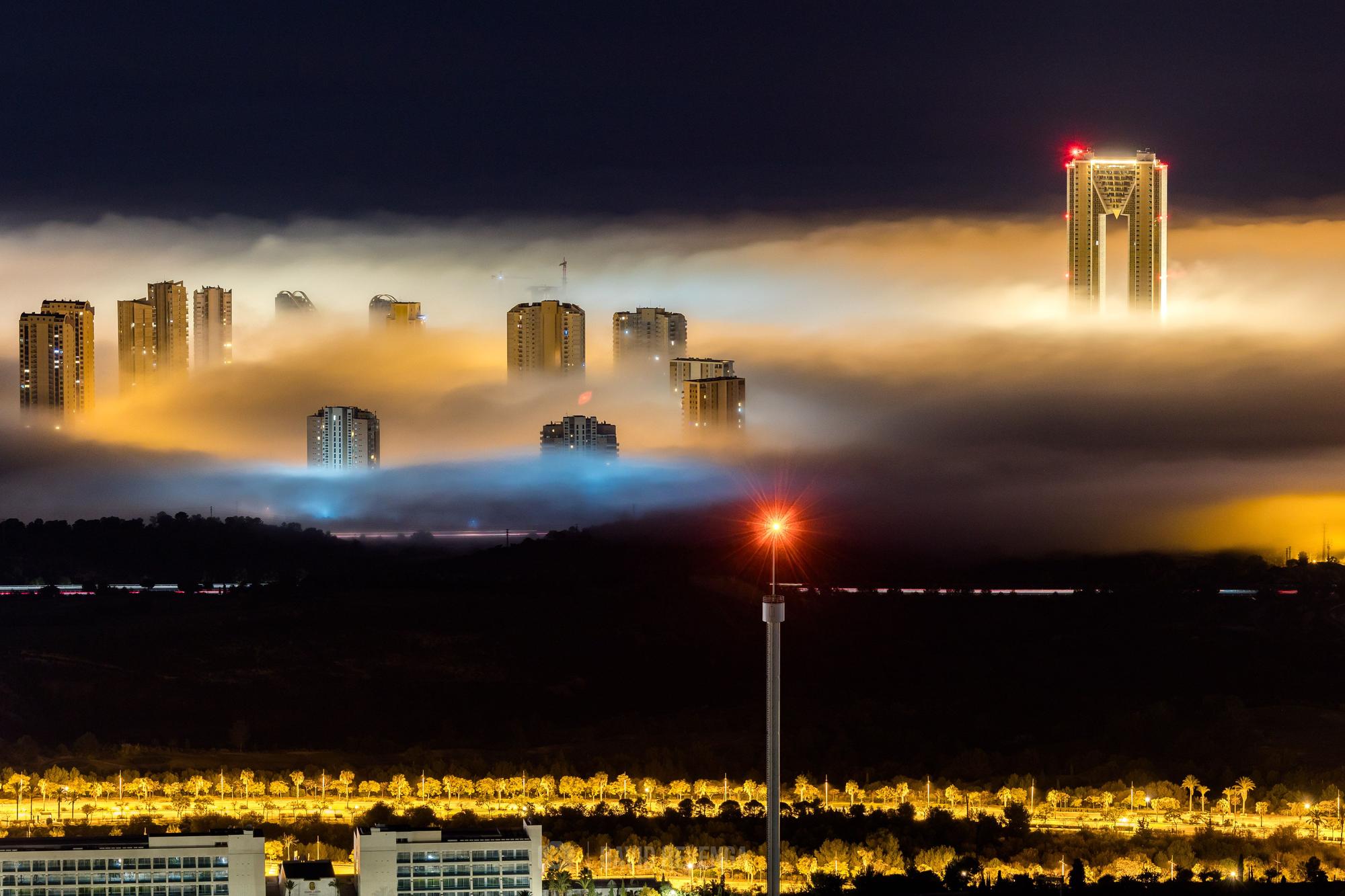 Una columna de niebla que ha entrado desde el mar ha "engullido" las playas y los edificios más cercanos a la primera línea de Benidorm, dejando imágenes del todo singulares de la ciudad.