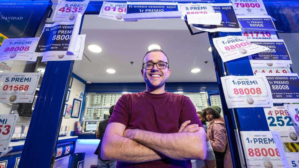 Víctor Fernández, el administrador de lotería de Las Arenas, en la entrada del negocio, empapelada con los carteles de los premios que acumuló en el sorteo de Navidad.