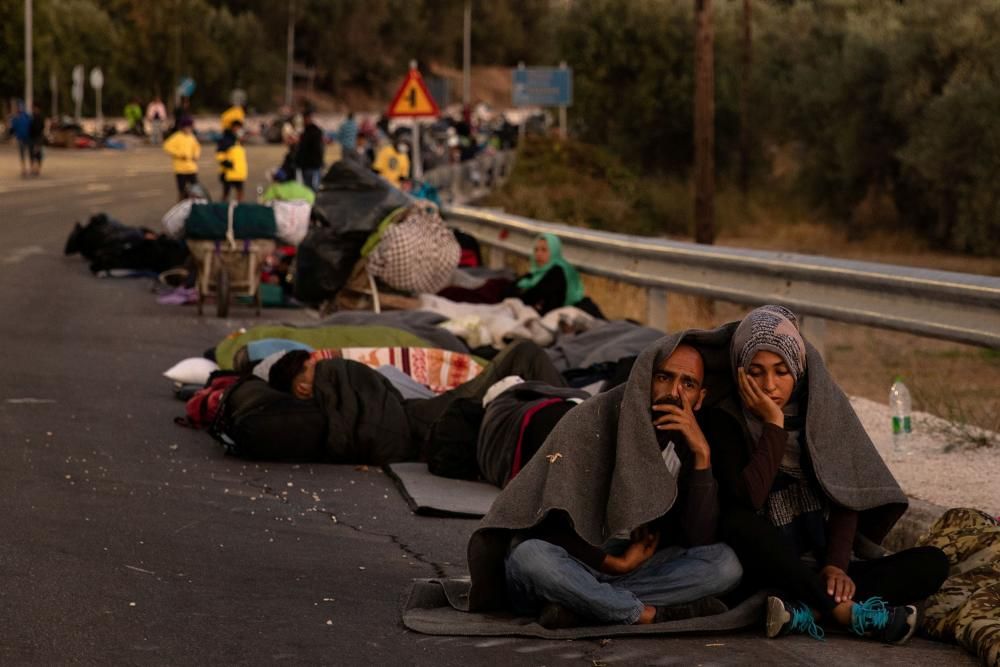 Couple sits covered with a blanket as refugees ...