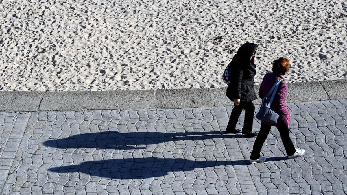 Dos mujeres caminan por el paseo marítimo de A Coruña un día soleado de otoño.