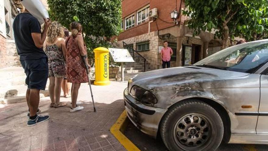 Las familias denunciantes junto al coche que intentaron quemarles y frente al Ayuntamiento de Agost con el alcalde al fondo.