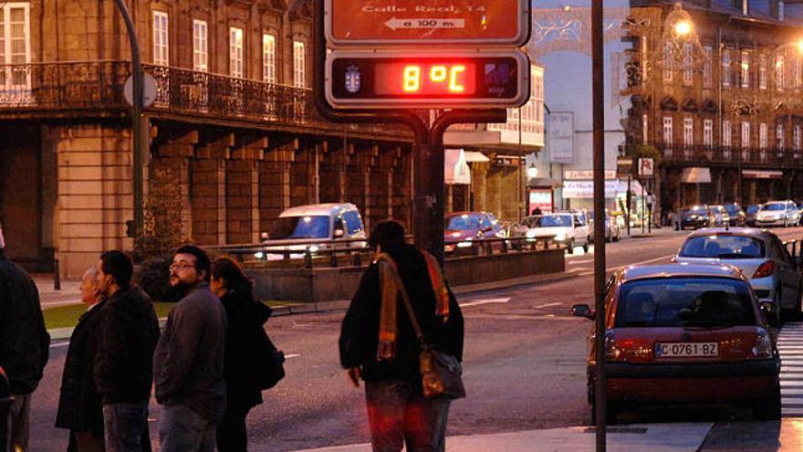 Varios coruñeses, ayer tarde, pasean abrigados ante un termómetro que marca 8 grados.