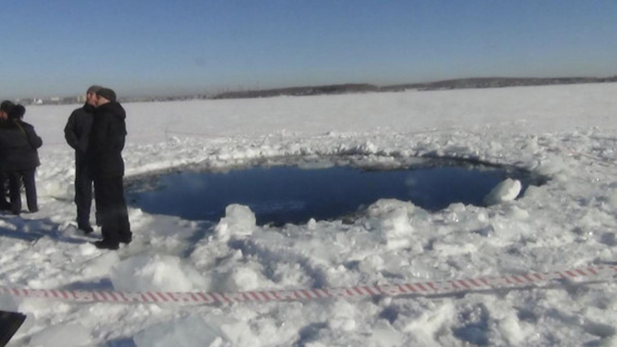 Varios hombres, junto a un agujero de ocho metros causado por el impacto del meteorito en un lago congelado de Cheliábinsk.