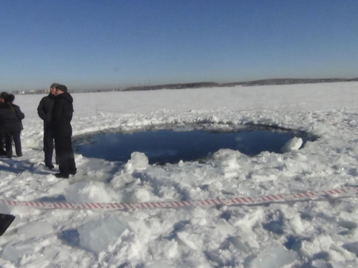 Diversos homes, al costat d’un forat de vuit metres causat per l’impacte del meteorit en un llac congelat de Chelyabinsk.