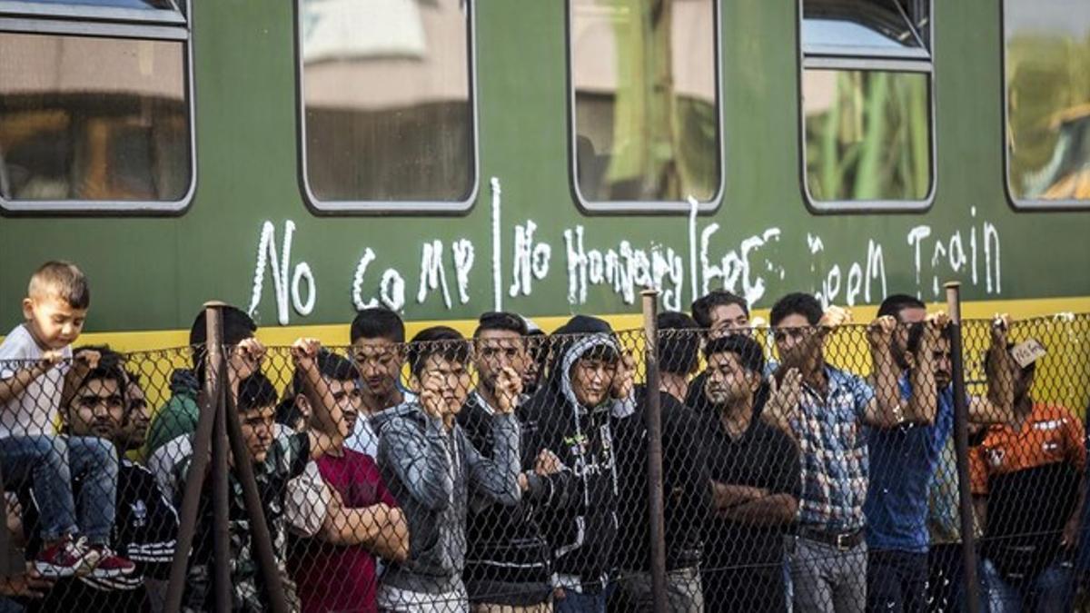 Grupos de refugiados piden continuar su viaje, junto a una valla frente al tren detenido, este viernes en Bcske.