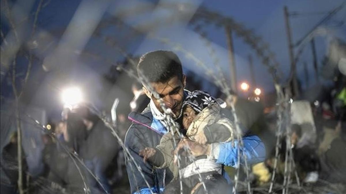 Un hombre afgano con su bebé en la frontera entre Grecia y Macedonia.