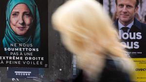 Una mujer pasa ante un carte electoral de Macron y Le Pen, ella con velo musulmán.