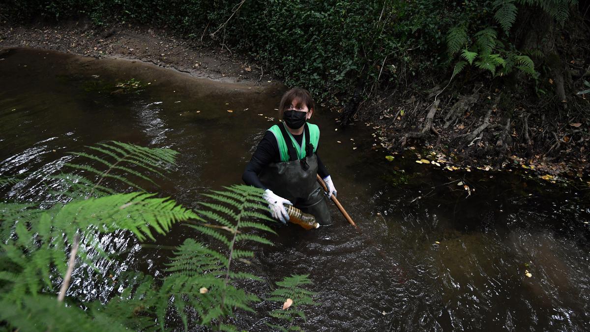 Una voluntaria retira una botella del río/ Gustavo Santos