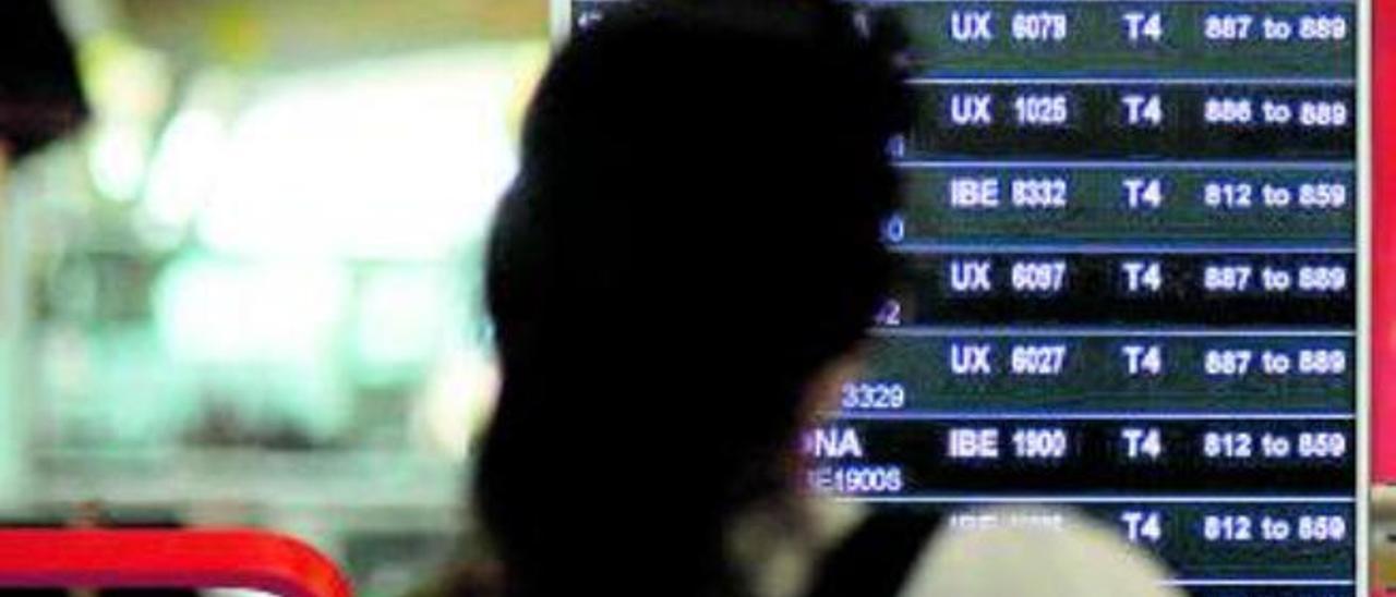 Una mujer observa un panel de vuelos en un aeropuerto.