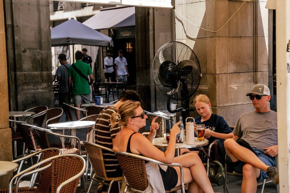 Una familia de turistas se refresca frente a un ventilador en una terraza en la Plaça Reial de Barcelona, esta semana.