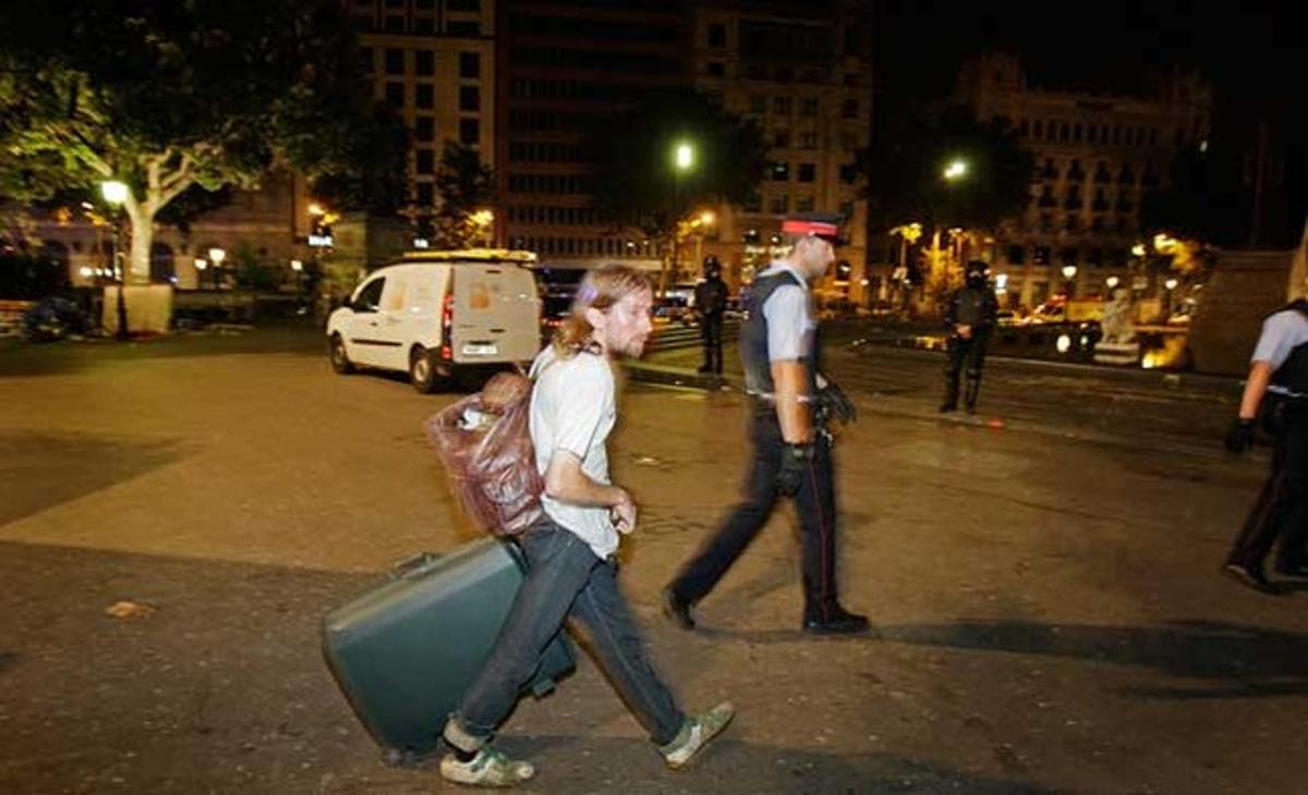 Un dels últims acampats de la plaça de Catalunya abandona tranquil·lament el recinte mentre arrossega una maleta.