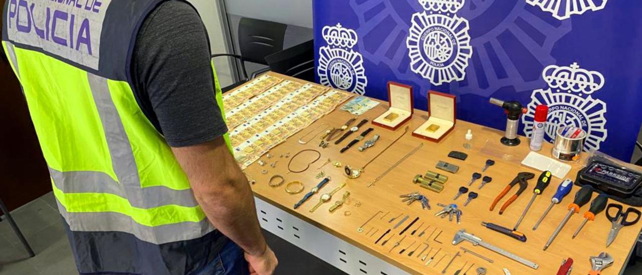 Un policía nacional junto al dinero, joyas y herramientas incautadas a los detenidos