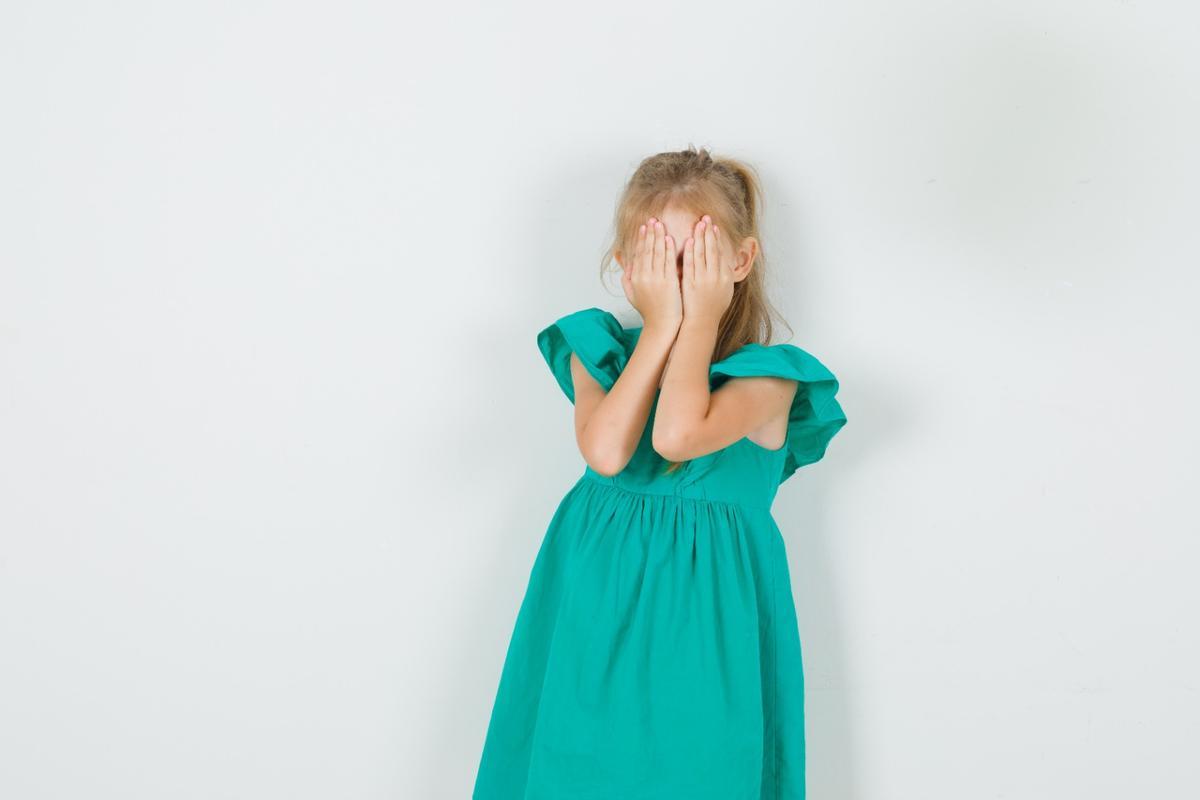 Una niña tapa su cara con las manos