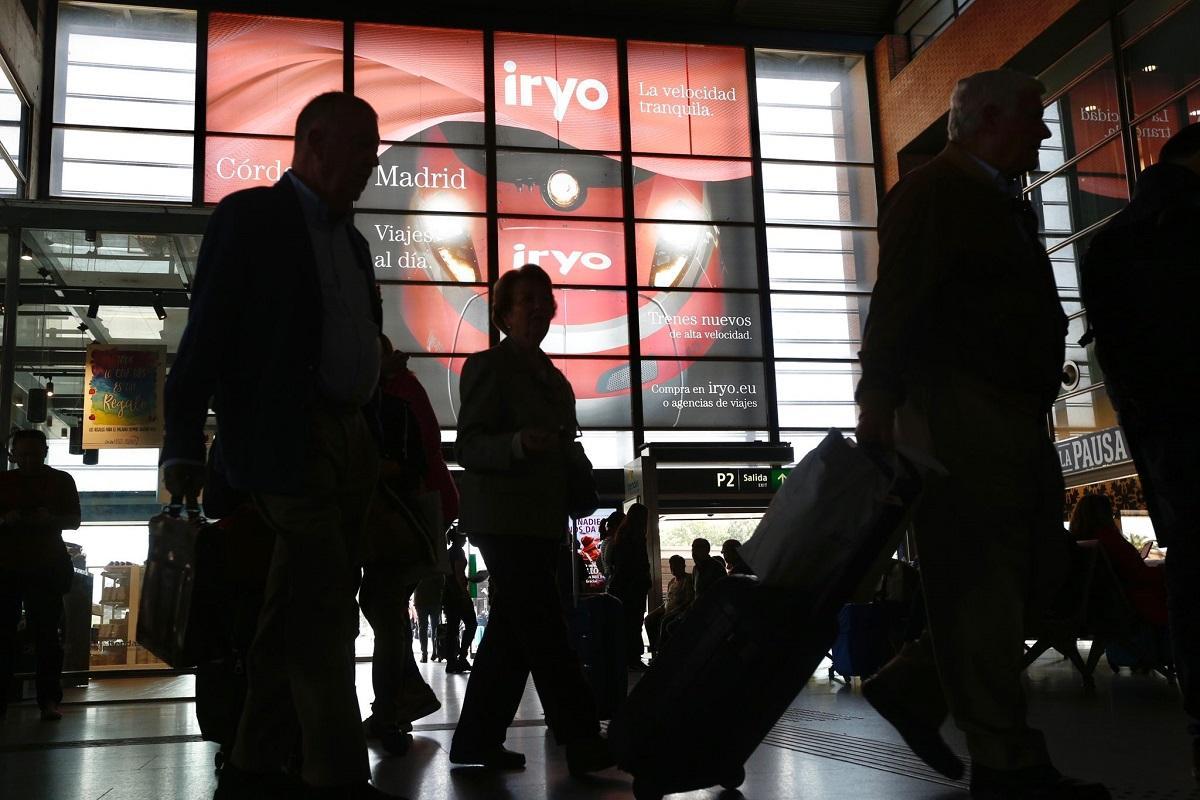 Viajeros en la estación de Córdoba, con la publicidad de los trenes de Iryo en los paneles de una de las entradas al edificio.