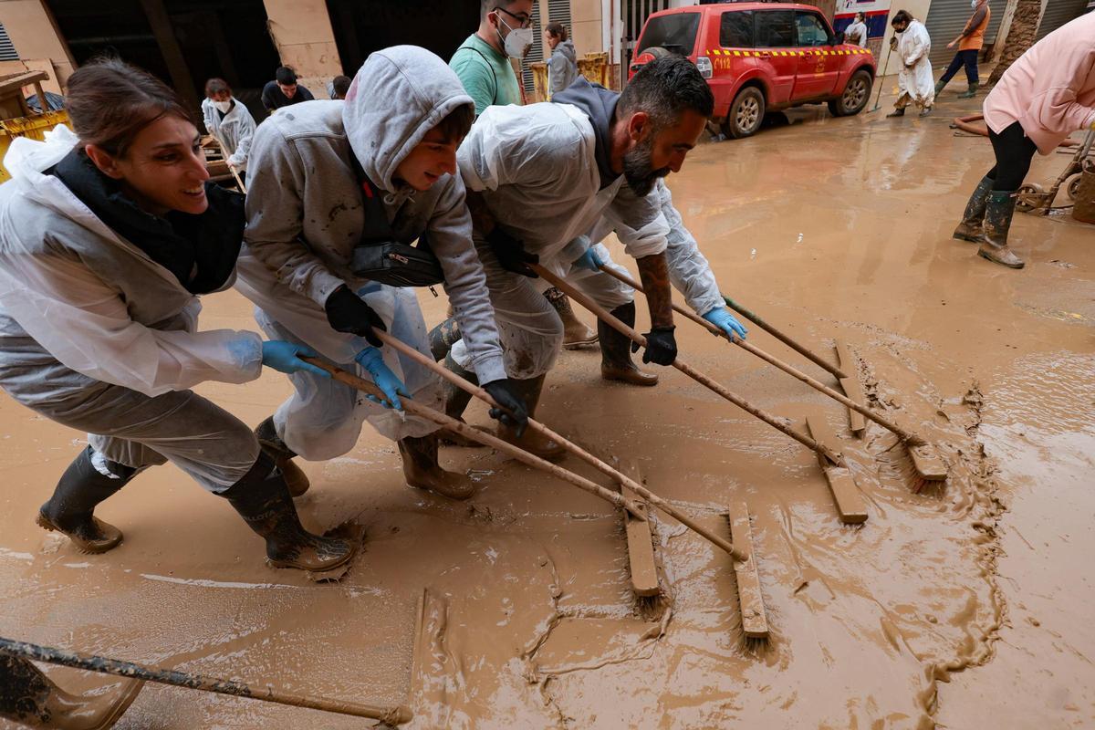 Un grupo de voluntarios tratan de apartar el barro de una calle de Paiporta, 18 días después de la dana.