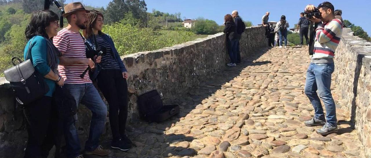 Unas turistas se fotografían con el gaiteru Serxu Luaces en el puente &quot;romano&quot; de Cangas de Onís.