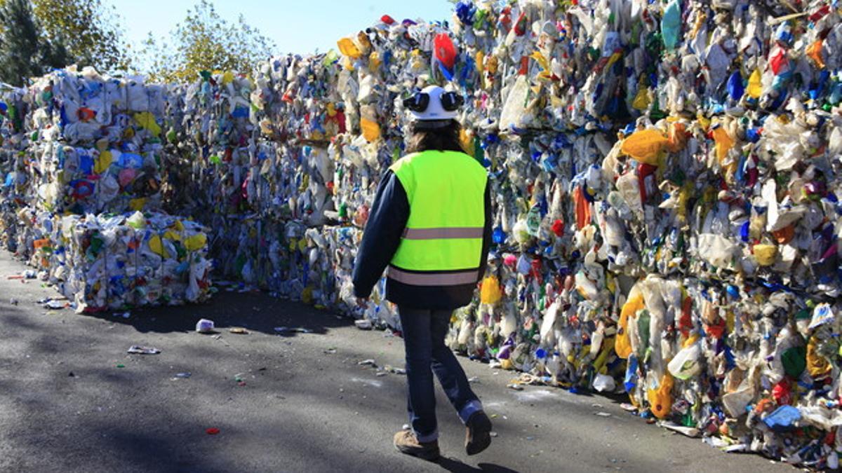 Una trabajadora del centro de tratamiento de residuos Les Valls, en Santa Maria de Palautordera, camina junto a una pila de plásticos.