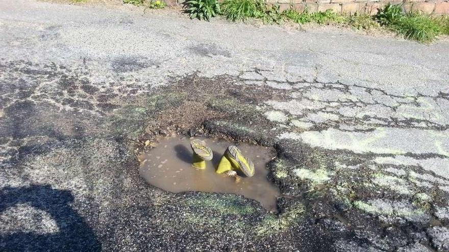 Unas botas simulan a un vecino &quot;buceando&quot; en los baches del vial de Seixo, en Darbo. // A.Vv. Daravelo