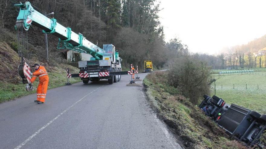 El camión volcado en Pravia, a la derecha, a punto de ser retirado por la grúa.