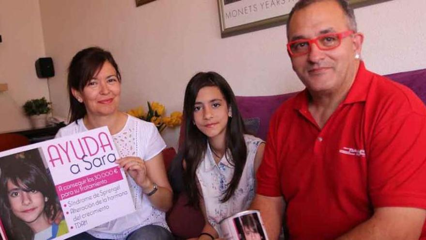 Sara junto a sus padres, Menchu Tejero y Víctor Gato, con uno de los carteles y una de las huchas repartidas para recoger fondos.