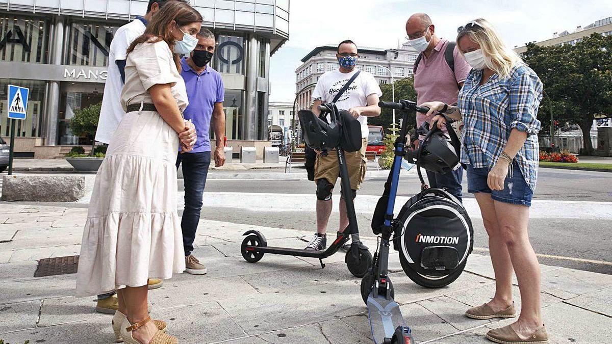 La alcaldesa, a la izquierda, observa unos patinetes eléctricos y a sus usuarios.